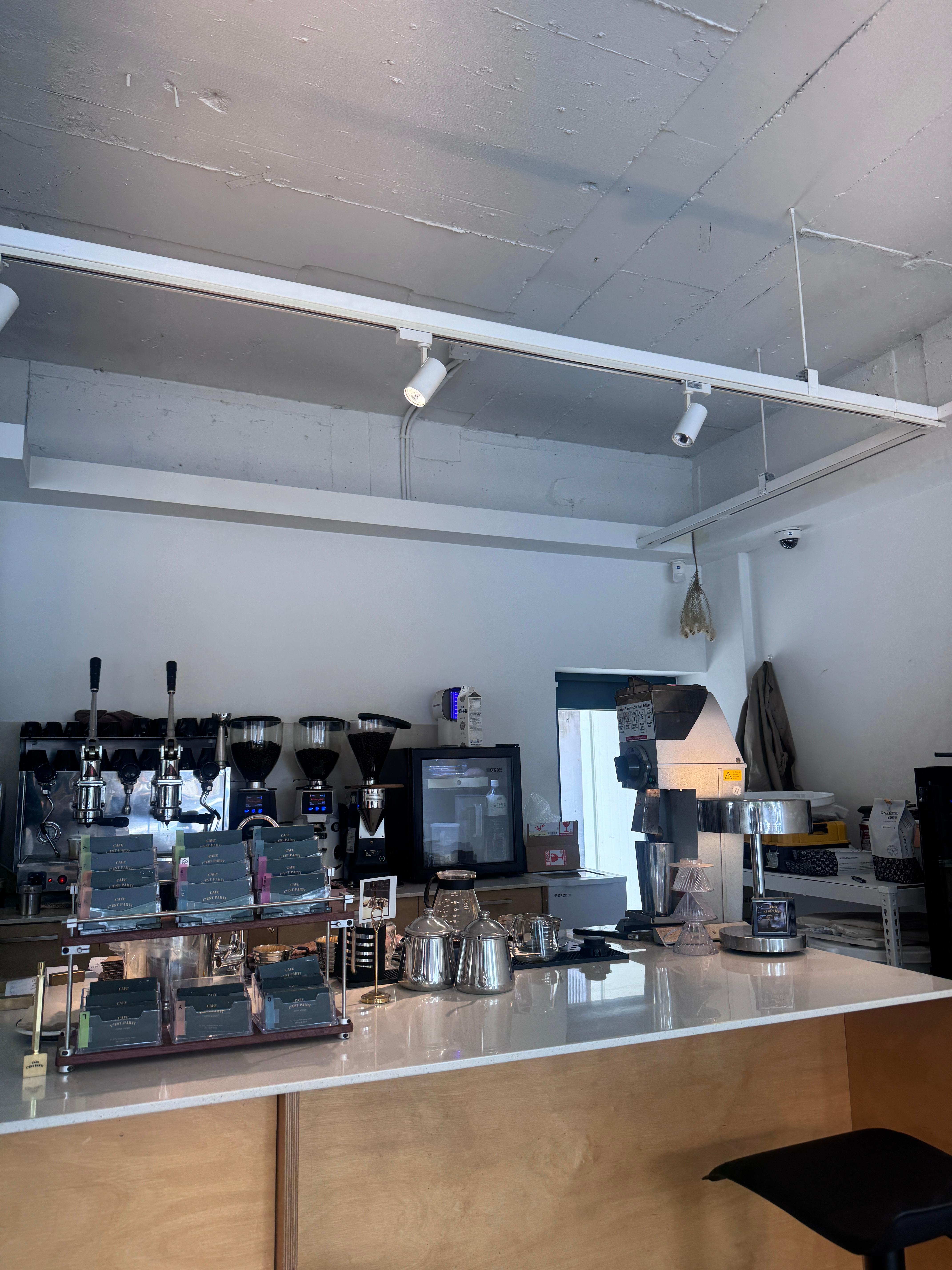 레버형 커피머신·그라인더·드리퍼·서버와 CAFE C’EST PARTI 포장이 진열된 커피바. 사람 없음.