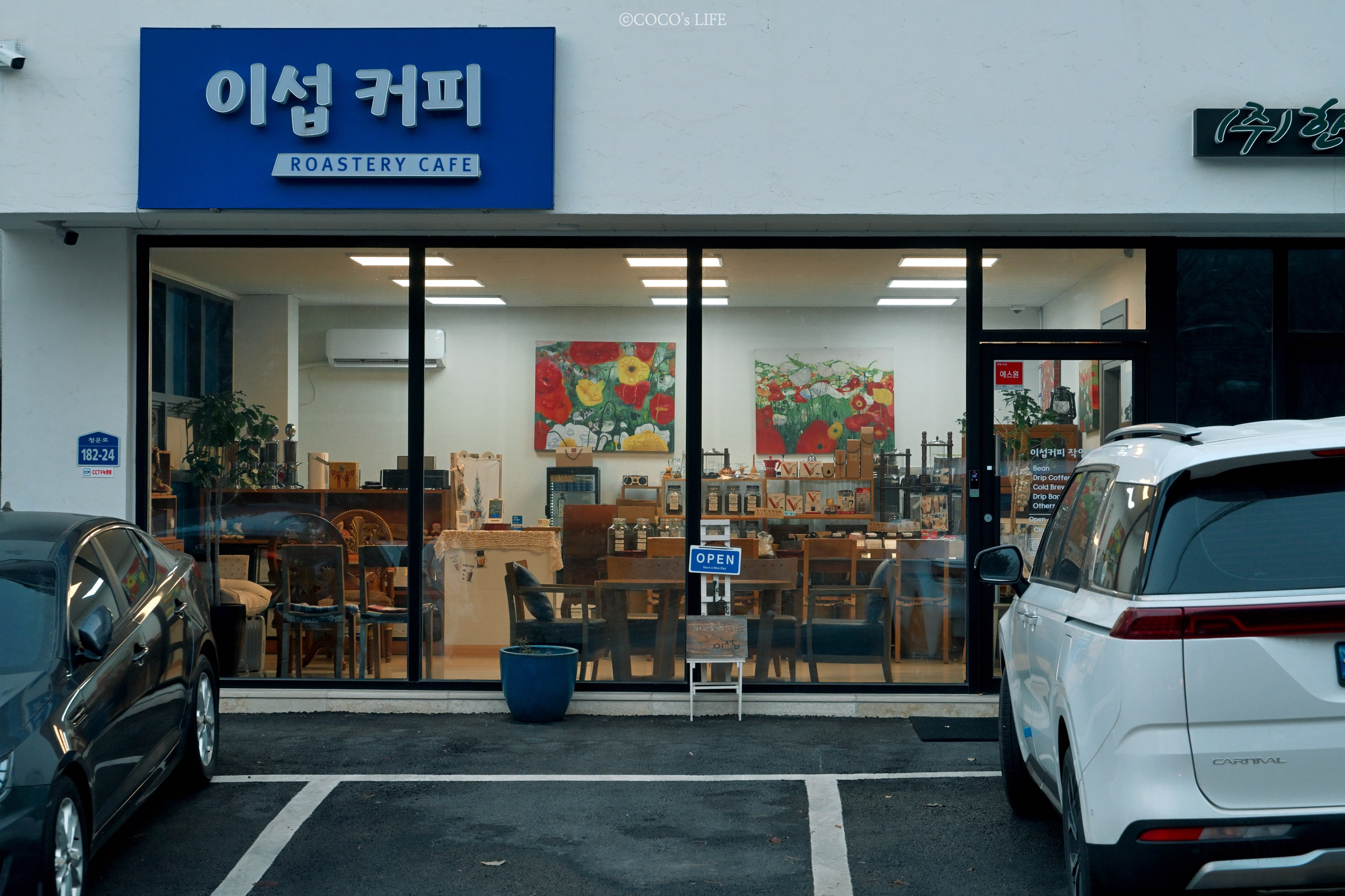파란 이섭커피 ROASTERY CAFE 간판, 왼쪽 182-24 주소판, 통유리 매장과 양쪽 주차 차량이 담긴 가로 외관 실사.