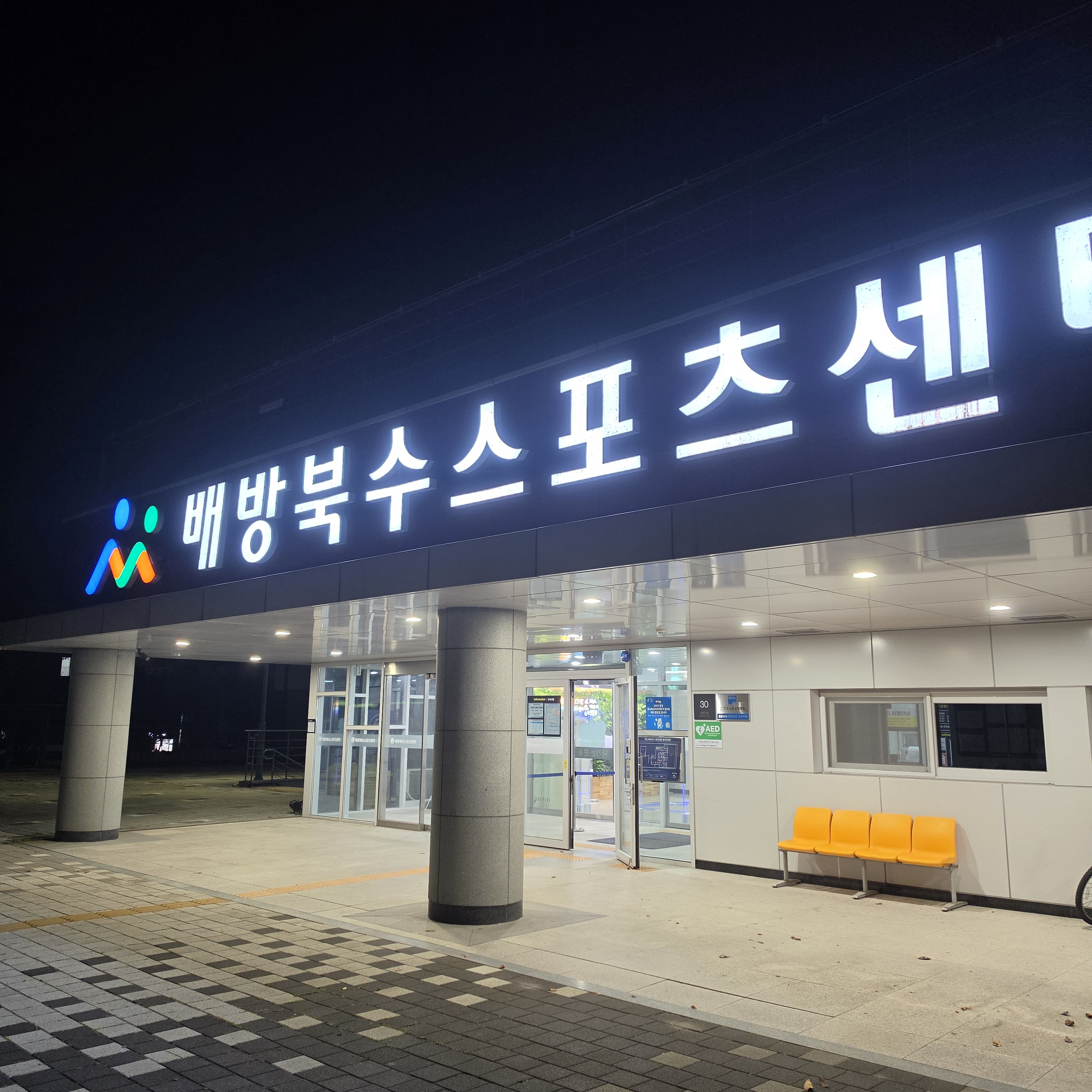 배방북수스포츠센터 야간 출입구와 조명 간판, 노란 의자