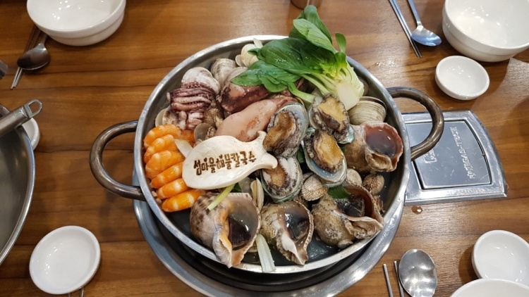 섬마을해물칼국수 상호가 찍힌 버섯과 조개류를 담은 냄비