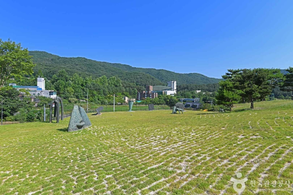 잔디와 격자형 바닥 너머 여러 조각과 산이 보이는 정원 · 자료사진