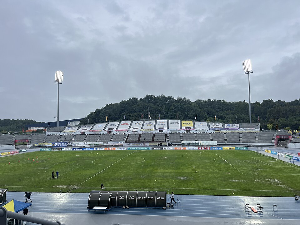 축구 피치 너머 회색 관중석과 조명탑이 보이는 이순신종합운동장 내부